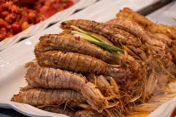 A platter of cooked and seasoned mantis shrimps, possibly in a pepper and salt style, garnished with green onions.

