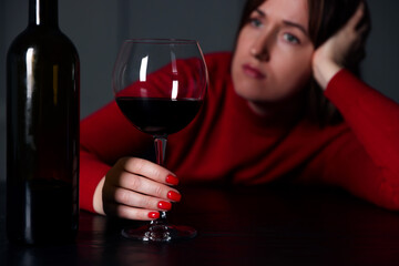 Alcohol addiction. Woman with glass of red wine and bottle at wooden table indoors, selective focus
