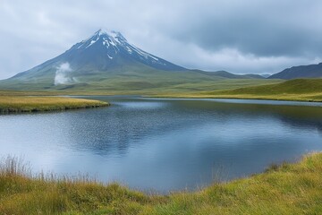 Majestic snow-capped mountain reflects in tranquil lake surrounded by lush green fields in a cloudy atmosphere