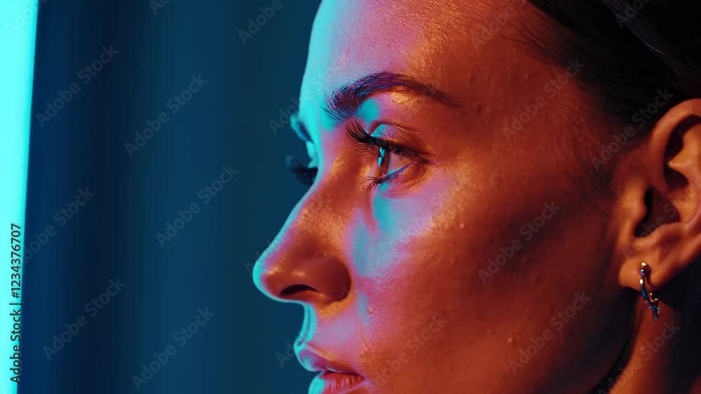 Poster a low-key shot focusing on the strong contrast between her focused expression and the neon-blue ambi