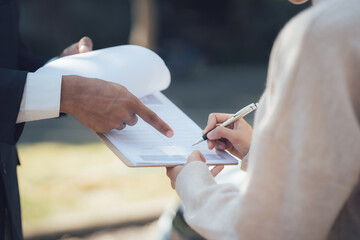 Fototapeta premium Signing a contract outdoors: A close-up shot showing hands of two people signing a document outdoors. One person is pointing to a specific section of the document. 