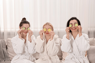 Happy women with cucumber slices on sofa in spa