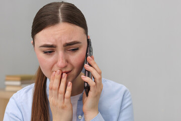 Stressed woman calling hotline for mental health help on grey background. Space for text