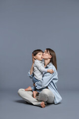 Mother kissing her little son on grey background. Space for text