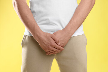 STD (sexually transmitted diseases). Man suffering from symptoms on yellow background, closeup