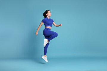Woman in sportswear exercising on light blue background