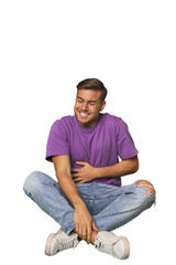 Obraz premium Casual man sitting on floor touches tummy, smiles gently, eating and satisfaction concept.