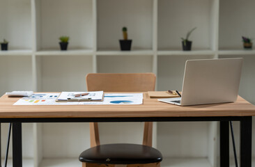 Minimalist Workspace:  A clean and tidy desk with a laptop, open notebooks, and a pencil, set against a backdrop of shelves with potted plants. The room is bathed in natural light.