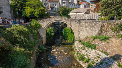 Crooked bridge seen from a drone. Small bridge in the streets of the tourist city of Mostar, Bosnia and Herzegovina. Characteristic bridge surrounded by nature and houses.