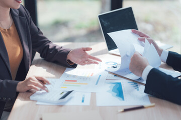Business Partners Reviewing Documents: Two business professionals collaborate closely, reviewing important financial documents and charts spread across a table.