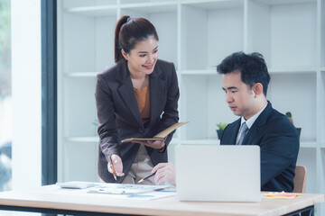 Focused Collaboration: Two colleagues, a woman in a brown blazer and a man in a suit, engaged in a productive conversation over a laptop and paperwork.