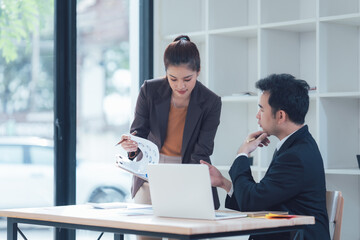 Business Analysis: A focused business meeting in a contemporary office setting, with a businesswoman presenting data on a chart to a male colleague.