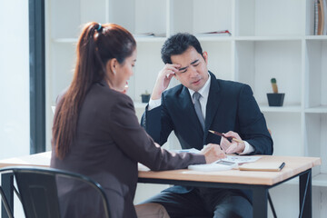 Serious Discussion: A pensive businessman and businesswoman engaged in a focused discussion at a desk, highlighting the gravity of their conversation and the importance of their work.