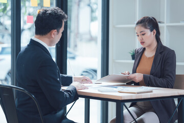 Business Meeting: A serious discussion unfolds between a male and female business professional in a modern office setting.  They're engrossed in reviewing documents.