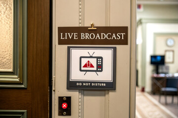 Sign indicating a live broadcast, featuring a warning message and a television graphic, positioned on a door in a professional setting.