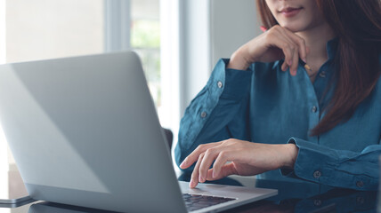 Fototapeta premium Business woman working on laptop computer at modern office. Pensive business woman thinking of problem solution, using laptop, planning and surfing the internet searching some ideas