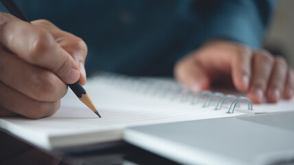 Close up, woman hand with pencil writing on spiral notebook with laptop computer on table, copy space for business background. business plan, e-learning, business and internet technology concept