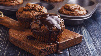 Chocolate muffins with chocolate syrup on dark background.