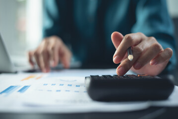 Business woman, accountant using calculator to calculate financial data, working on laptop computer with business document on office table, doing finance, budgeting and cost control, business concept