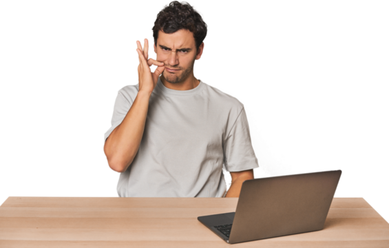 Hispanic young man working on laptop with fingers on lips keeping a secret.