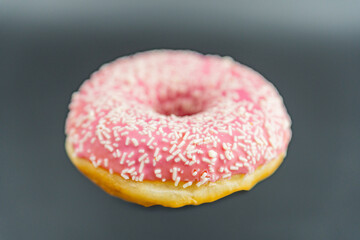 A brightly lit image of a single pink-glazed doughnut adorned with matching pink sprinkles, set against a neutral backdrop