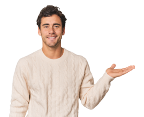 Young Hispanic man in studio showing a copy space on a palm and holding another hand on waist.