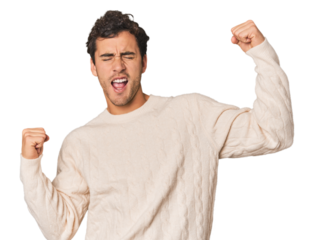 Young Hispanic man in studio raising fist after a victory, winner concept.