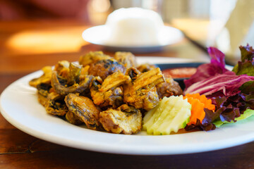 Deep fried shiitake mushrooms wtih wheat flour, thai style food with fresh vegetables on white plate in warm light of morning. Blurry steamed rice background. Vegan and healthy food concept.
