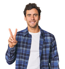 Young Hispanic man in studio joyful and carefree showing a peace symbol with fingers.