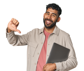 Hispanic male holding laptop in studio showing a dislike gesture, thumbs down. Disagreement concept.
