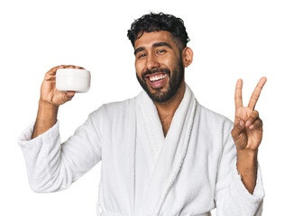 Hispanic male with moisturizer in studio joyful and carefree showing a peace symbol with fingers.