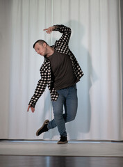 Young guy in a dancing pose on a white background. Modern dance in a plaid shirt. Sports plastic movements of arms and legs and body.