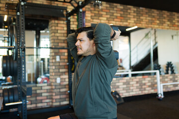 Mid adult chubby man performing triceps workouts with dumbbells in a modern gym, focusing on strength training and fitness goals