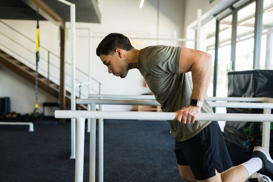 Strong sportsman exercising on parallel bars, building upper body strength in modern fitness center