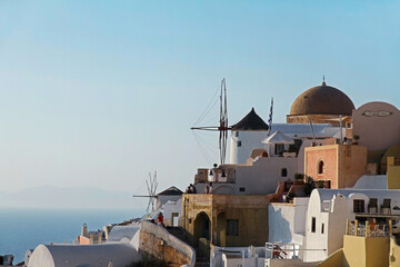 Picturesque view of the traditional white houses and windmills on the mountainside in Oia on the blue sky background taken closeup.