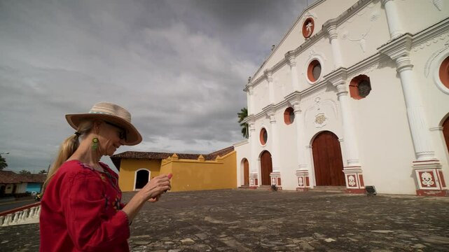 A mature woman enjoys her time in Granada, Nicaragua, capturing the stunning architecture of the convent and church with her smartphone while taking in the experience.