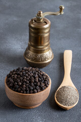 A bowl of black peppercorns on a black background and a metal grinder