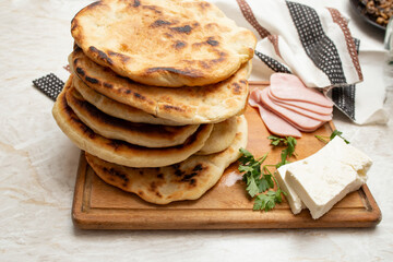 Fried pita bread stack on a wooden chopping board with ham slices and goat cheese, cococi, turte, scovergi