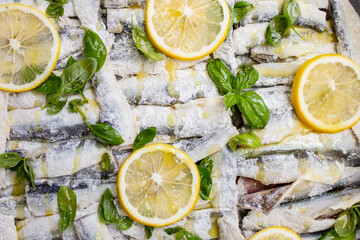 Baby hering fish stacked in a tray with olive oil , basil leaves and lemon slices, soft focus side...