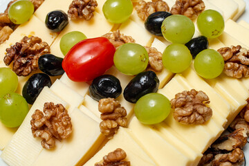 Finger food plate with walnut halves, cheese slices and grapes, soft focus close up