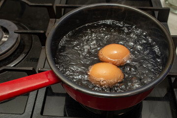 Two orange eggs boiling in a  black pot with bubbles and steam, soft focus  close up
