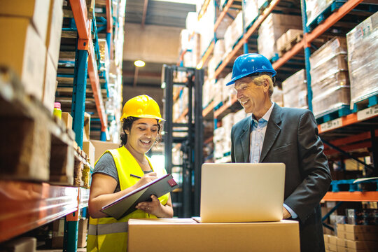 Warehouse manager and female worker discussing inventory logistics with clipboard and laptop