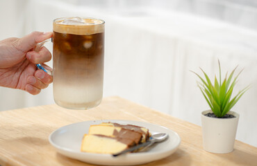Close up and selective focus hand of man holding glass of ice coffee on wooden table