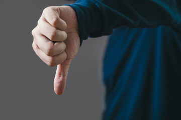 A close-up image of a hand displaying a thumbs-down gesture against a neutral background,...