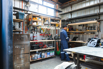 Latin mechanic working on laptop in organized workshop with tools and equipment