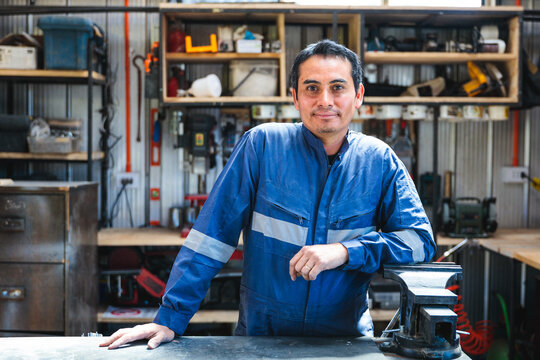 Portrait of confident Latin carpenter or craftsman posing in his workshop with tools and vise