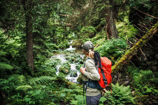 Woman hiker with backpack enjoying view to stream in forest. Hiking and exploration in nature