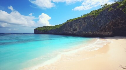 Fototapeta premium A beautiful turquoise sea meets a sandy beach, backed by a rocky cliff with green vegetation under a blue sky