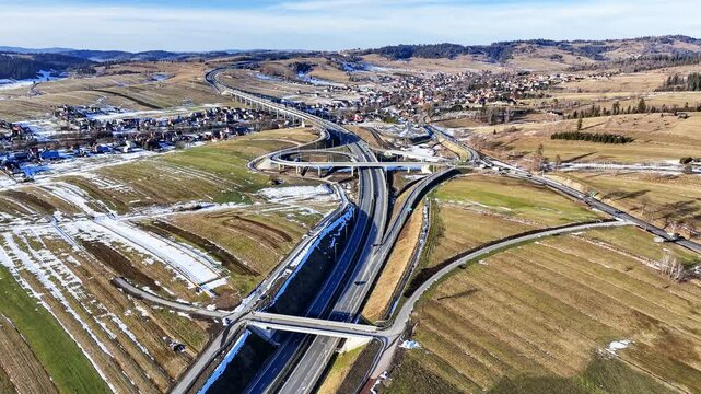 New highway interchange on Zakopianka motorway with ramps, viaduct and traffic circle, joining the new highway with old road. Viaduct over Klikuszowa village  Aerial approaching 4K video. January 2025