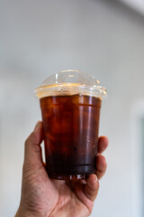 Hand holding a cup of iced black coffee drink, close up